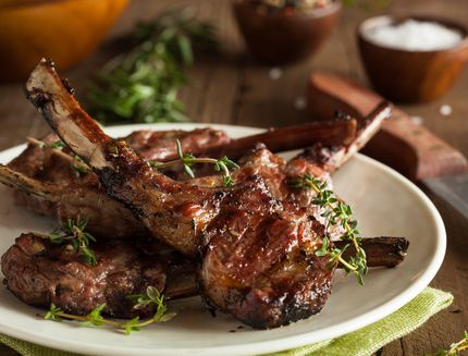 Grilled lamb chops organized on a white plate on wood