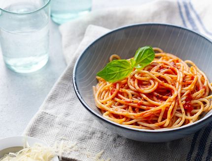 Pasta, spaghetti with tomato sauce and fresh basil in a bowl. Grey background. Copy space.